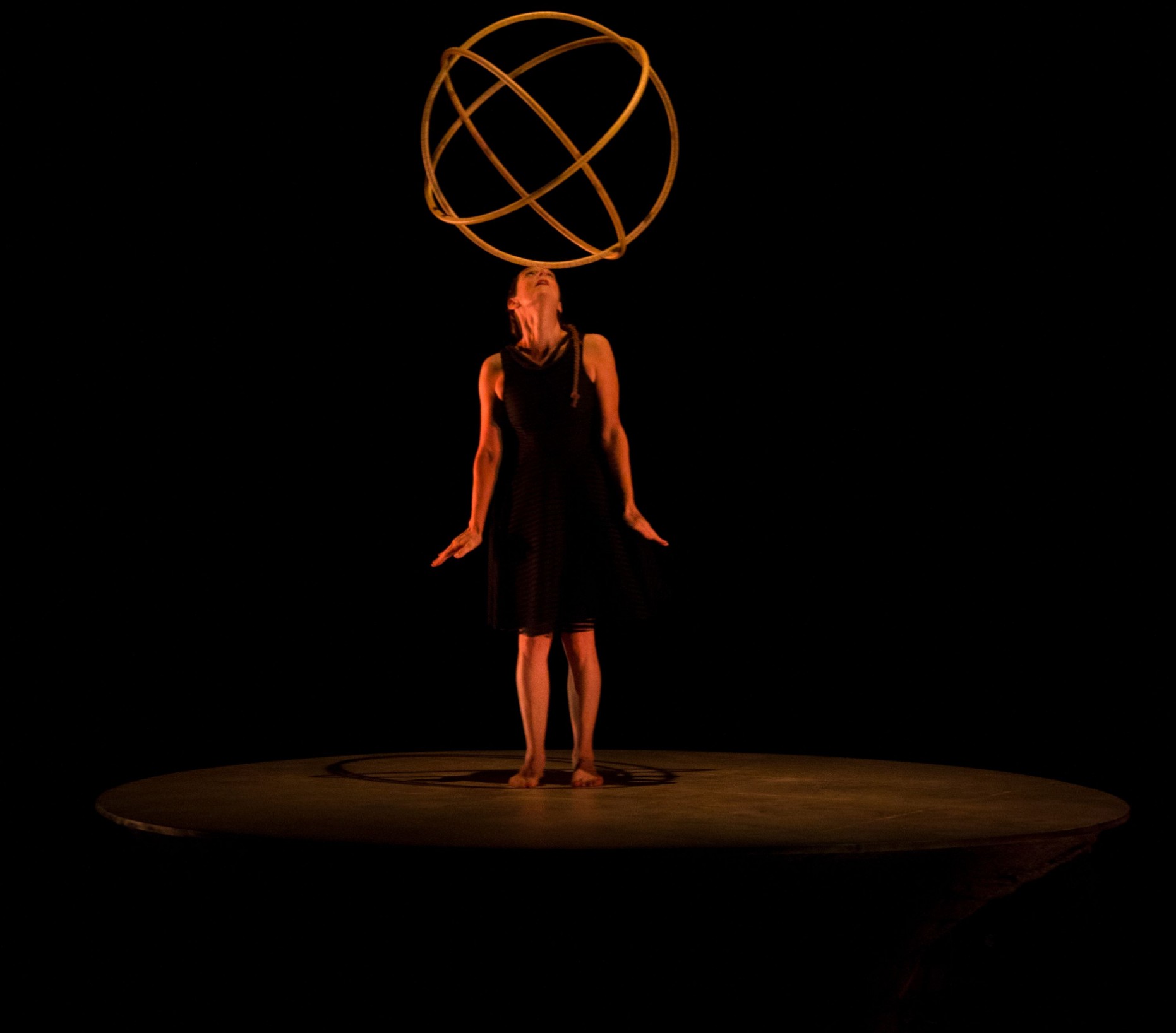 Karen Bourre Jongleuse debou sur le planète tient en équilibre sur son front trois hula hoop emboités en sphère lumière sombre et chaude